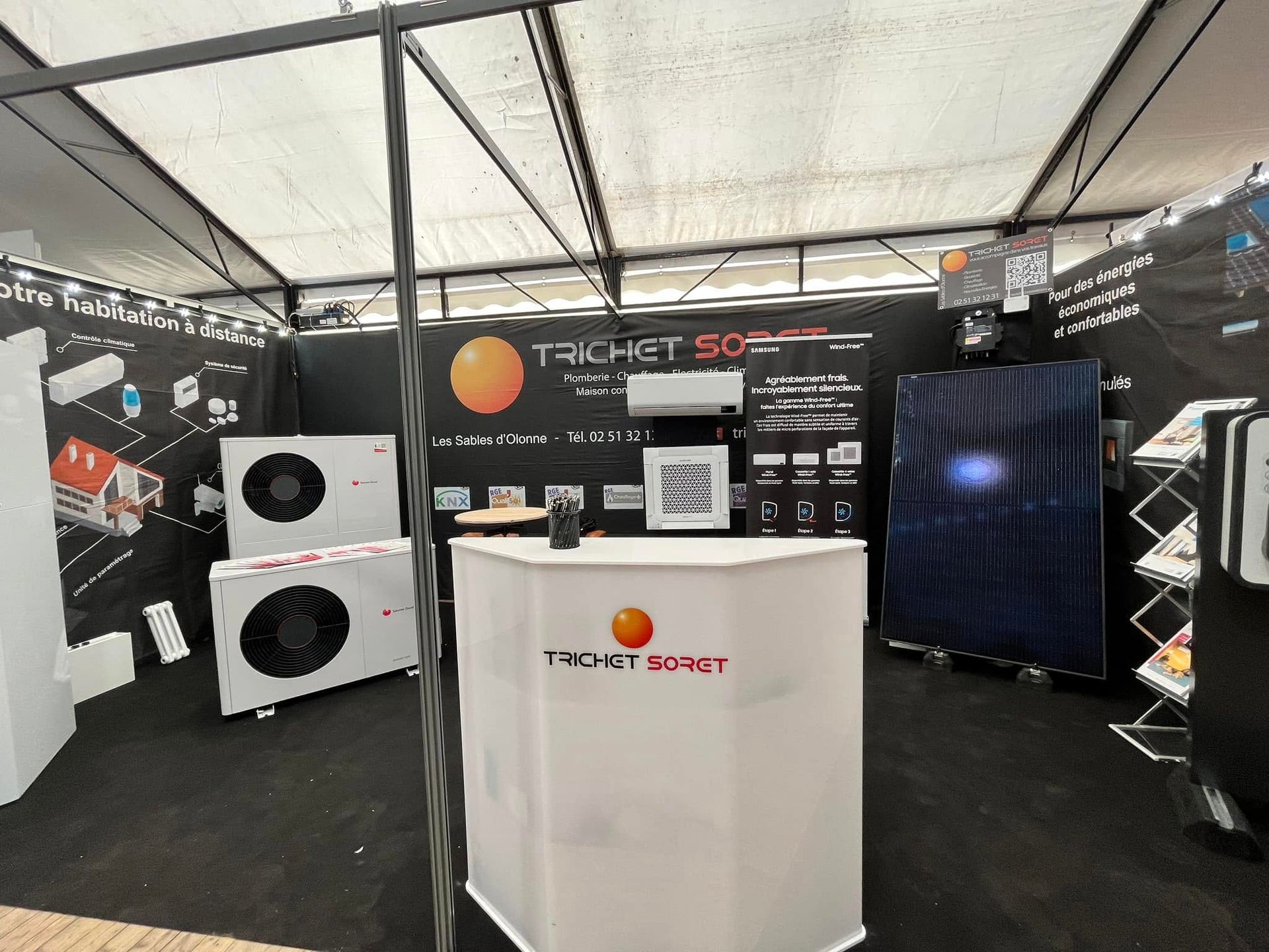 Un stand d'exposition pour Trichet Soret présentant des pompes à chaleur, un présentoir de panneaux solaires et un comptoir promotionnel blanc.