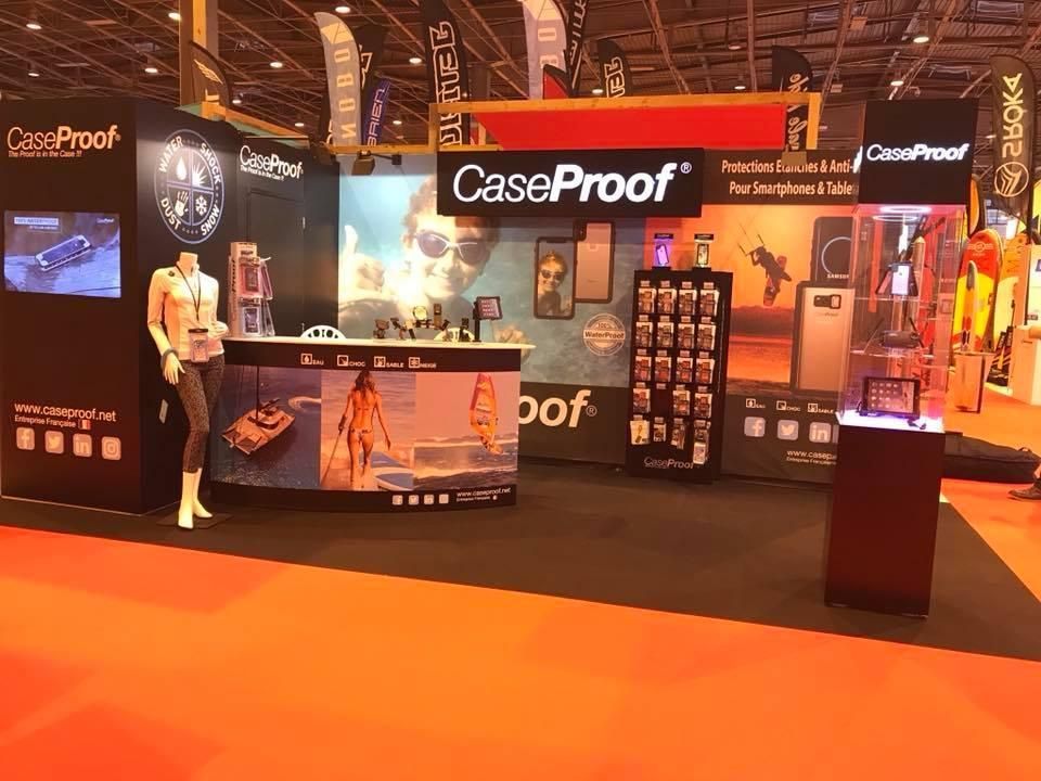 Un stand CaseProof aux couleurs de la marque présente des produits, un mannequin et des images promotionnelles sur un tapis orange.