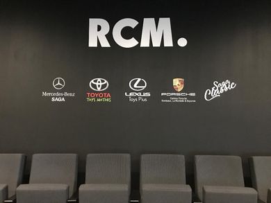 Un mur noir avec l'inscription RCM au-dessus de cinq logos de marques et une rangée de sièges gris en dessous.