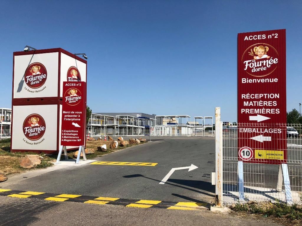 Une entrée de site industriel La Fournée Dorée avec signalisation rouge, flèches directionnelles et marquages ​​de limitation de vitesse.