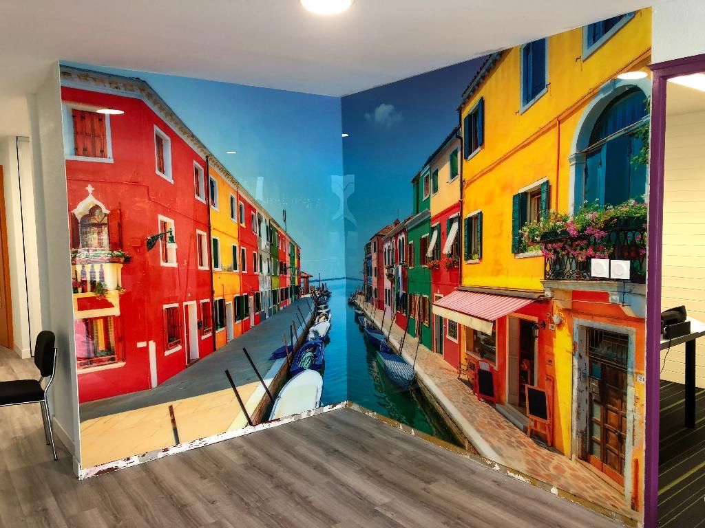 Fresque murale montrant des bâtiments colorés bordant un canal sur deux murs qui se croisent dans une pièce.