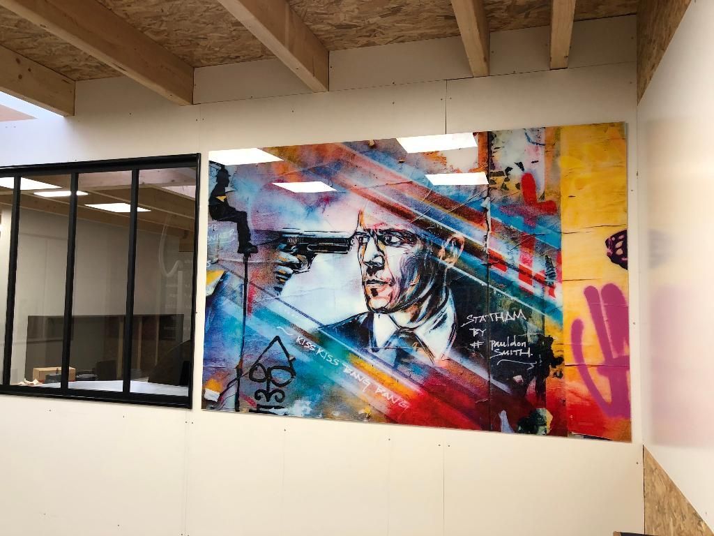 Une fresque murale sur un mur blanc représente un homme en costume entouré de graffitis abstraits et vibrants dans des tons de bleu, de rouge et de jaune.