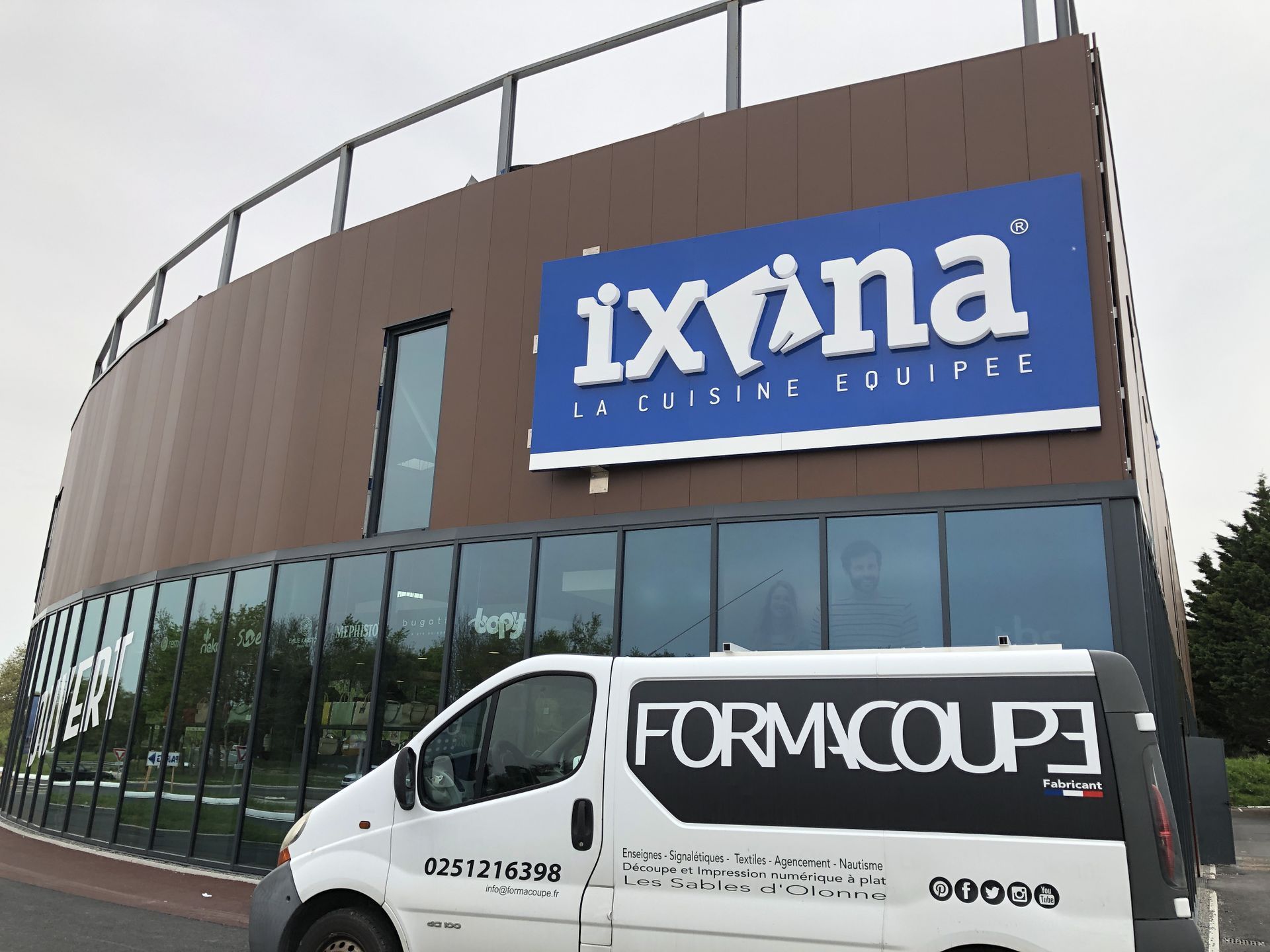 Une camionnette FMC Formacoupe blanche garée devant un bâtiment moderne arborant une grande enseigne bleue Ixina sur sa façade marron.