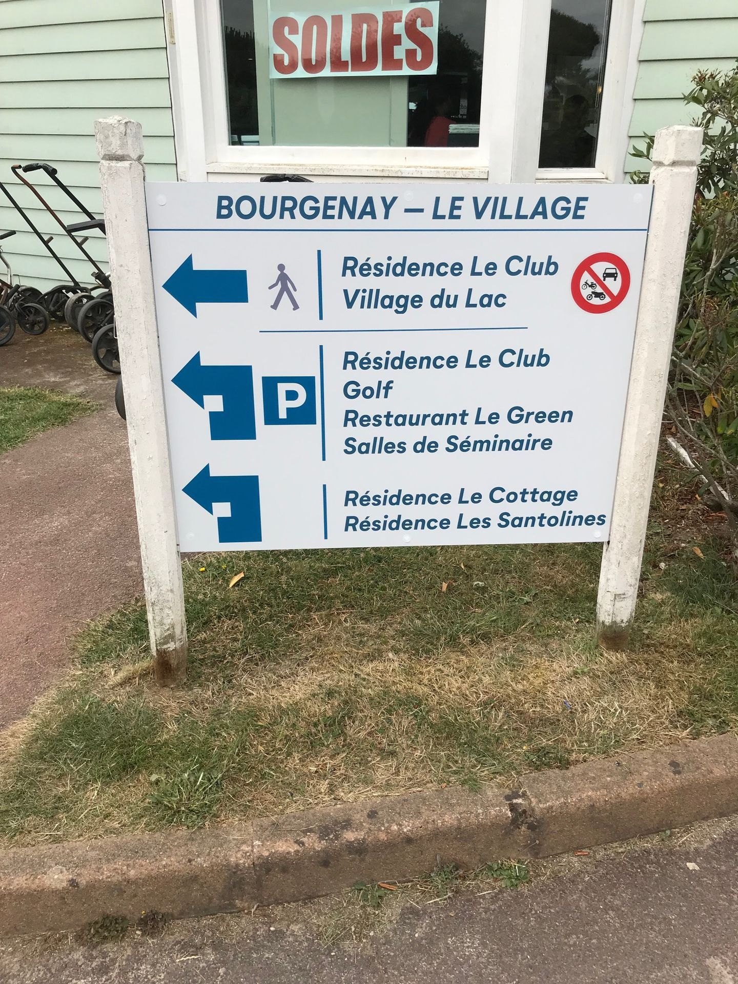 Un panneau blanc avec des inscriptions bleues et des flèches indiquant aux piétons et aux automobilistes la direction de différentes habitations, d'un restaurant et d'une boîte de nuit.