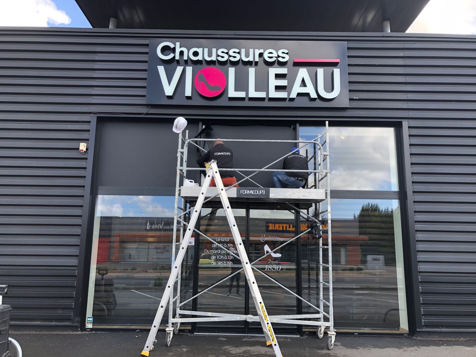 Enseigne extérieure sur un bâtiment en métal noir pour Ligne Carrée, une entreprise de carrelage, comportant des éléments de logo carrés et colorés.