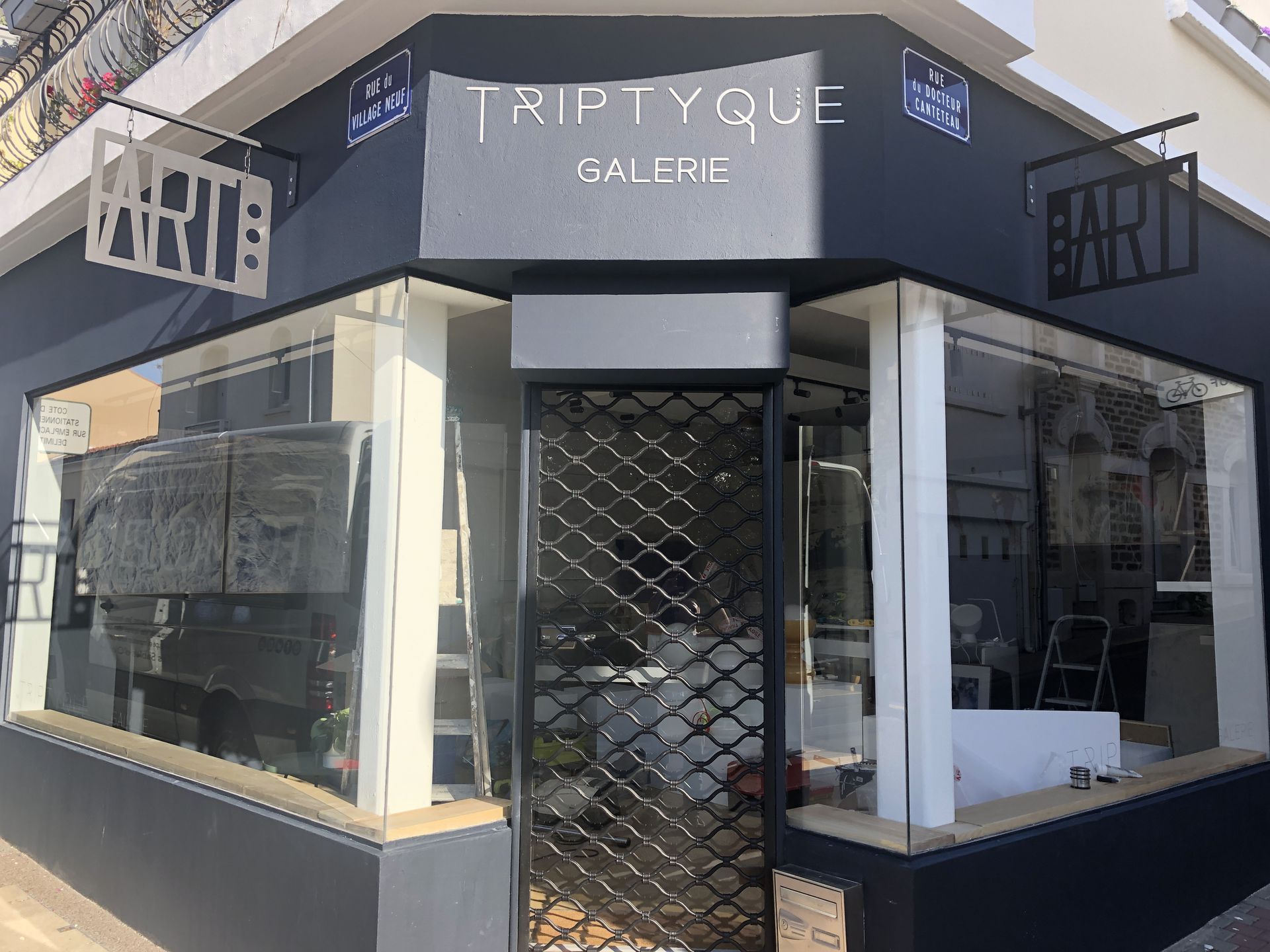 La façade d'angle de la galerie Triptyque, de couleur gris foncé, avec des vitrines et un portail de sécurité en métal.