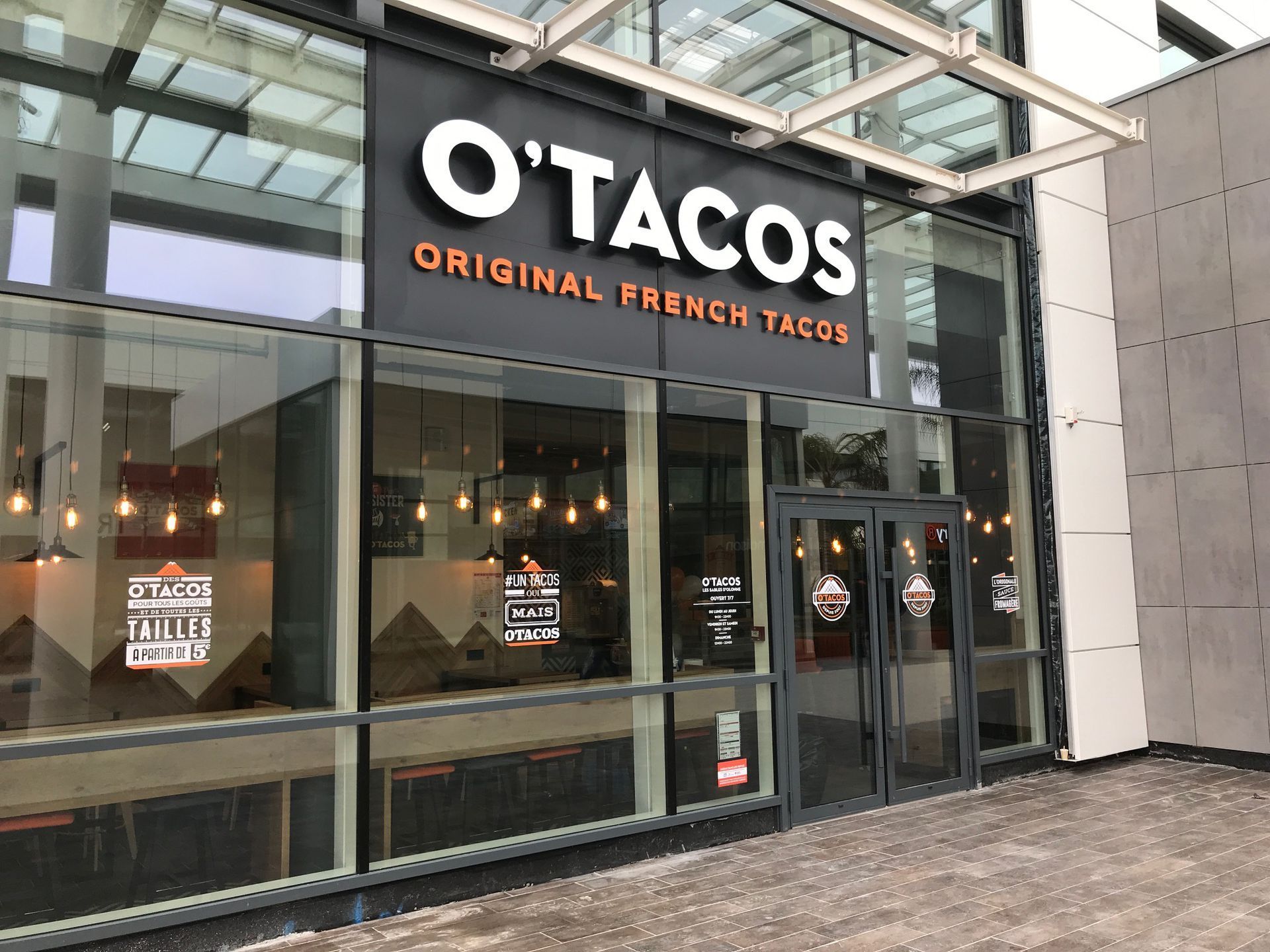 La façade d'un restaurant O'Tacos, avec une grande enseigne noire à texte blanc et des vitrines.