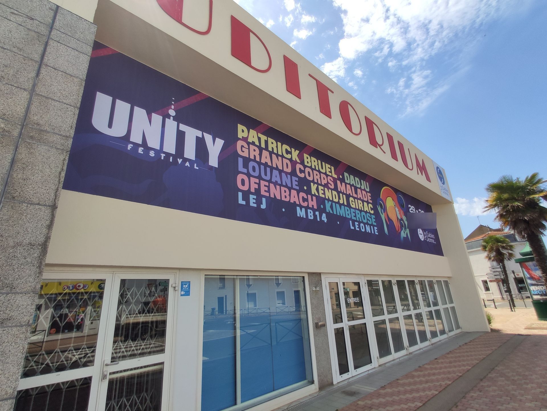 Une façade d'immeuble avec une banderole Unity Festival listant des artistes comme Patrick Bruel et Louane au-dessus de l'entrée.