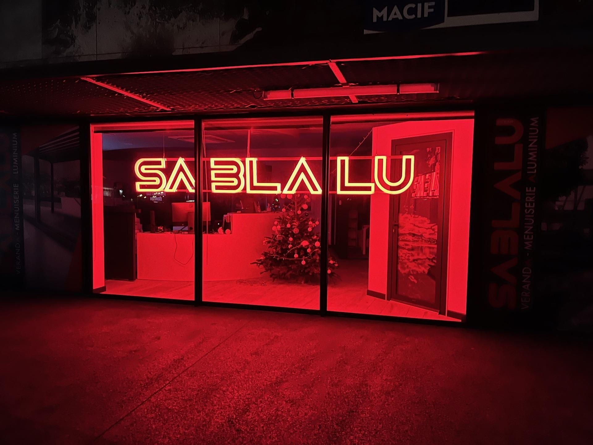 L'intérieur d'une boutique, baigné de lumière rouge la nuit, présente une enseigne lumineuse au néon.