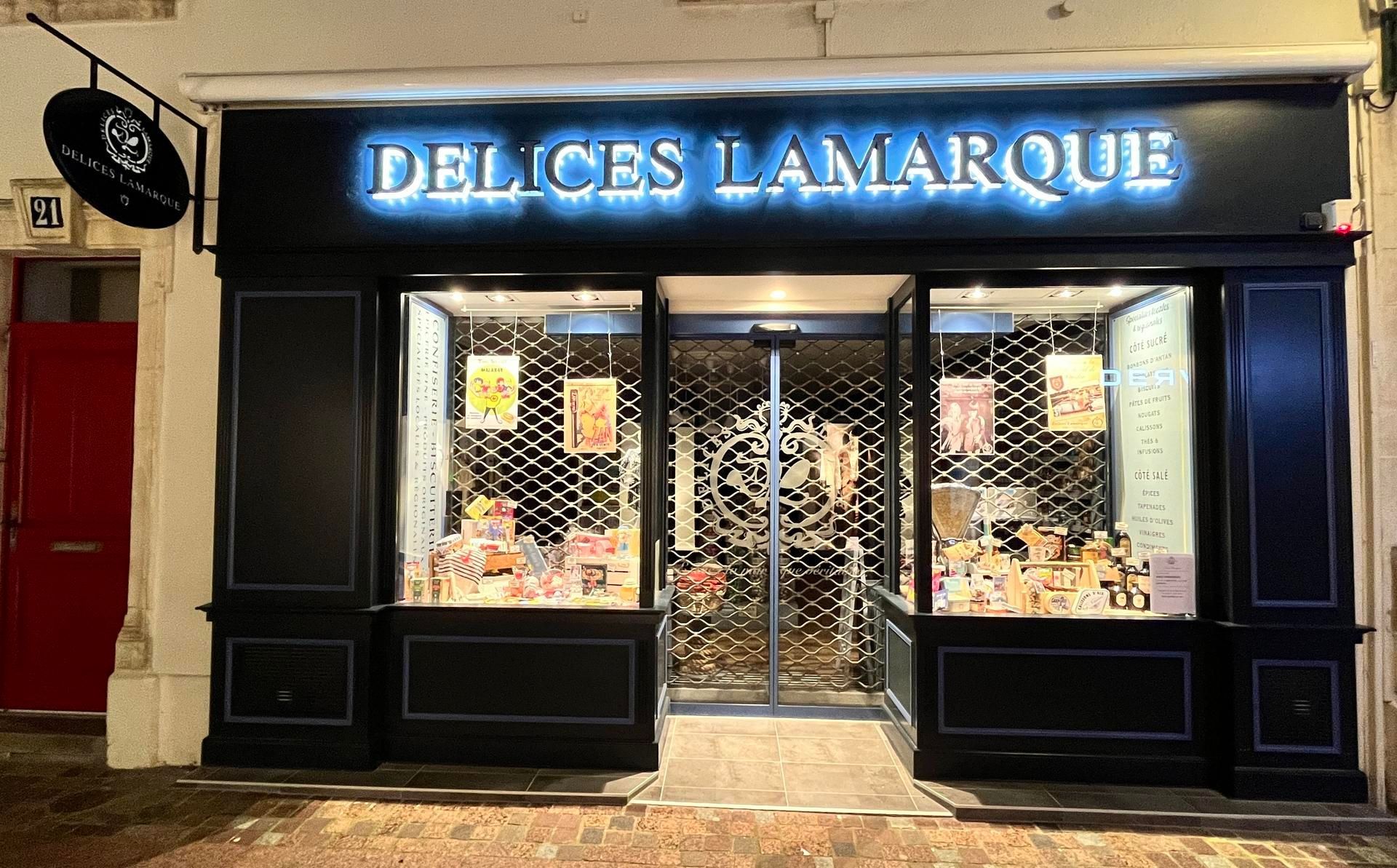 Façade du magasin Délices Lamarque la nuit, avec sa façade sombre, son enseigne lumineuse et sa vitrine.