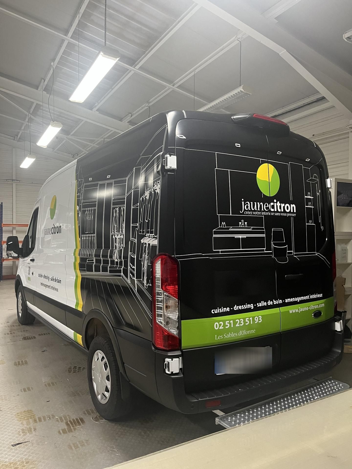 Une camionnette blanche et noire avec des inscriptions vertes est garée dans un garage, affichant un logo et un schéma technique de machinerie.