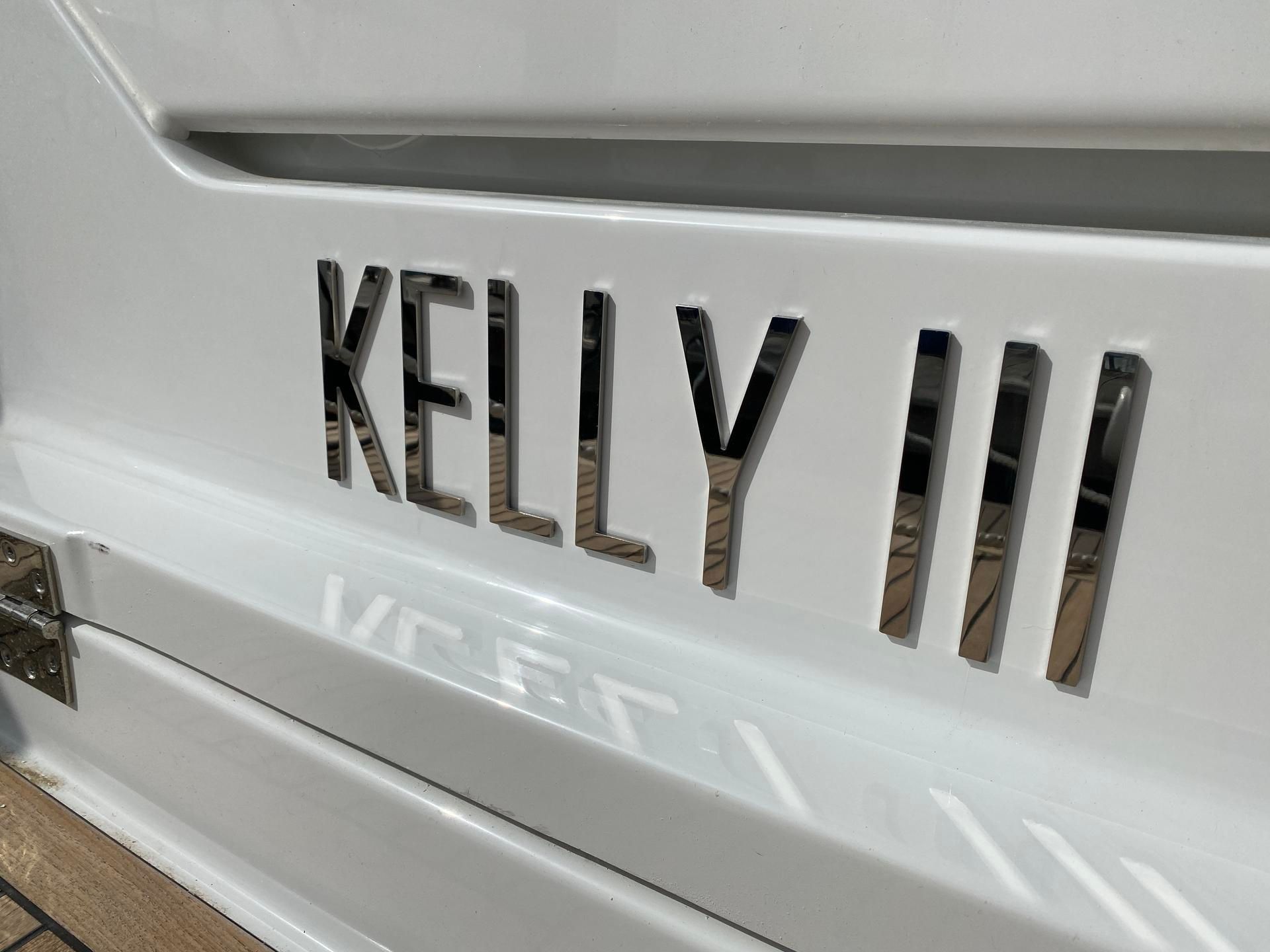 Le nom chromé poli KELLY III est apposé sur la coque blanche brillante d'un bateau.