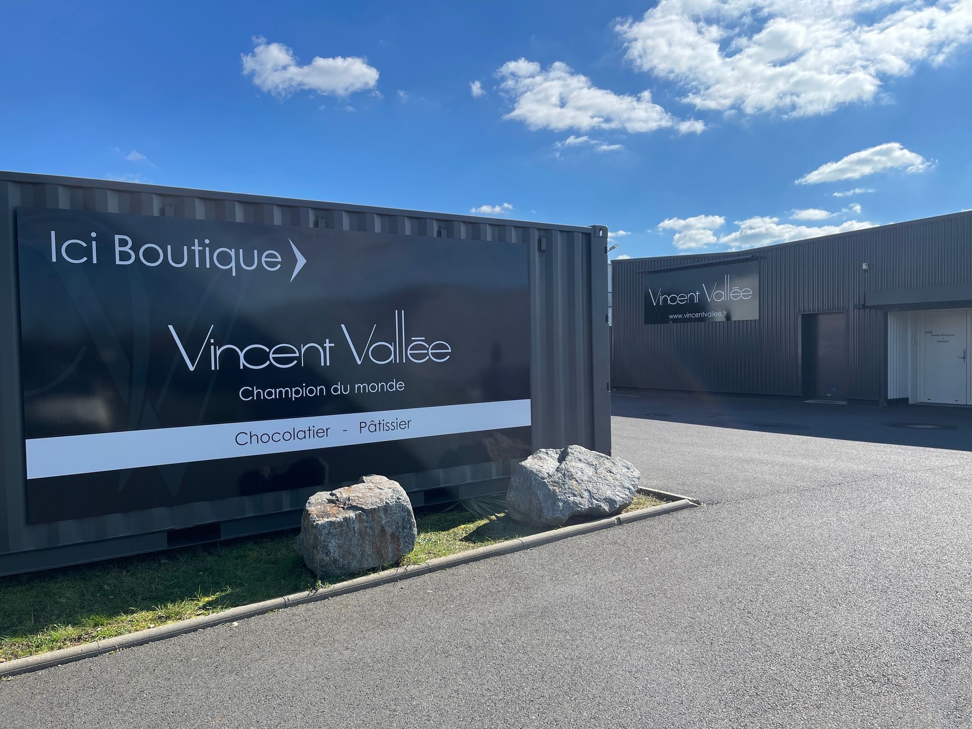 Vue d'angle d'un bâtiment moderne à façade vitrée arborant le logo 37DEUX L'agence sous un ciel bleu clair.