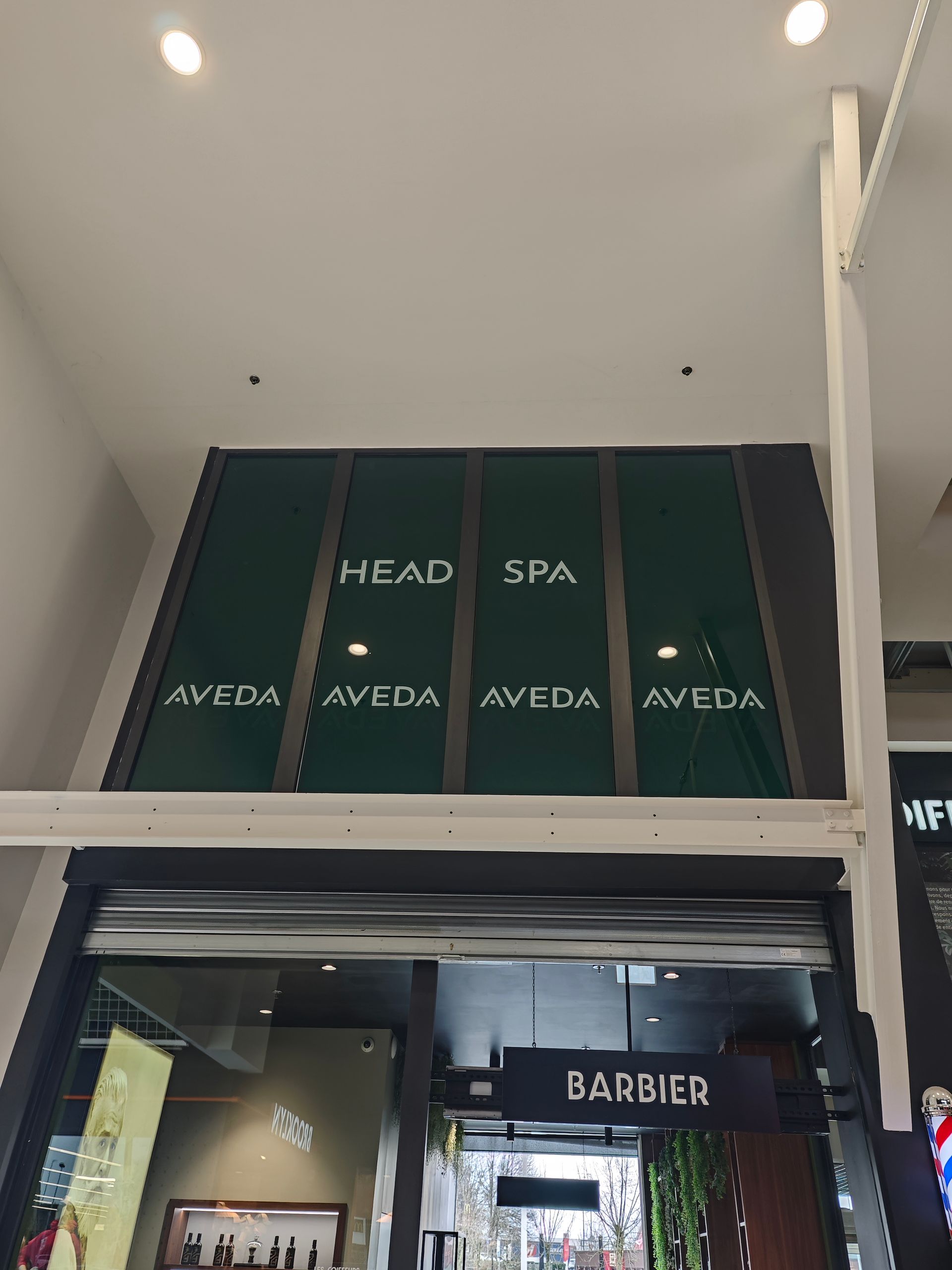 Une enseigne métallique pour immeuble de bureaux, avec du texte sur un mur extérieur texturé gris clair, à côté d'une porte.