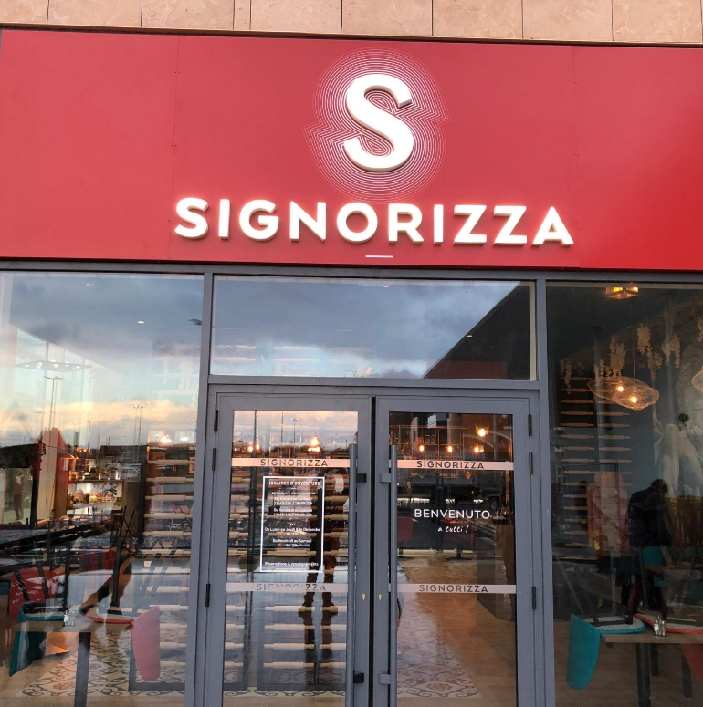 La façade d'un restaurant Signorizza arborant une enseigne rouge vif avec un texte blanc et un logo S blanc stylisé.