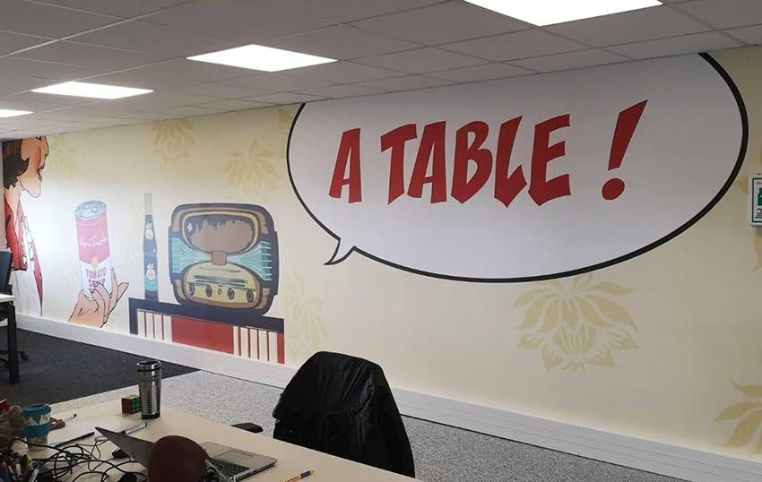 Mur de bureau orné d'une fresque murale représentant une télévision rétro et d'une bulle de dialogue disant : UNE TABLE !