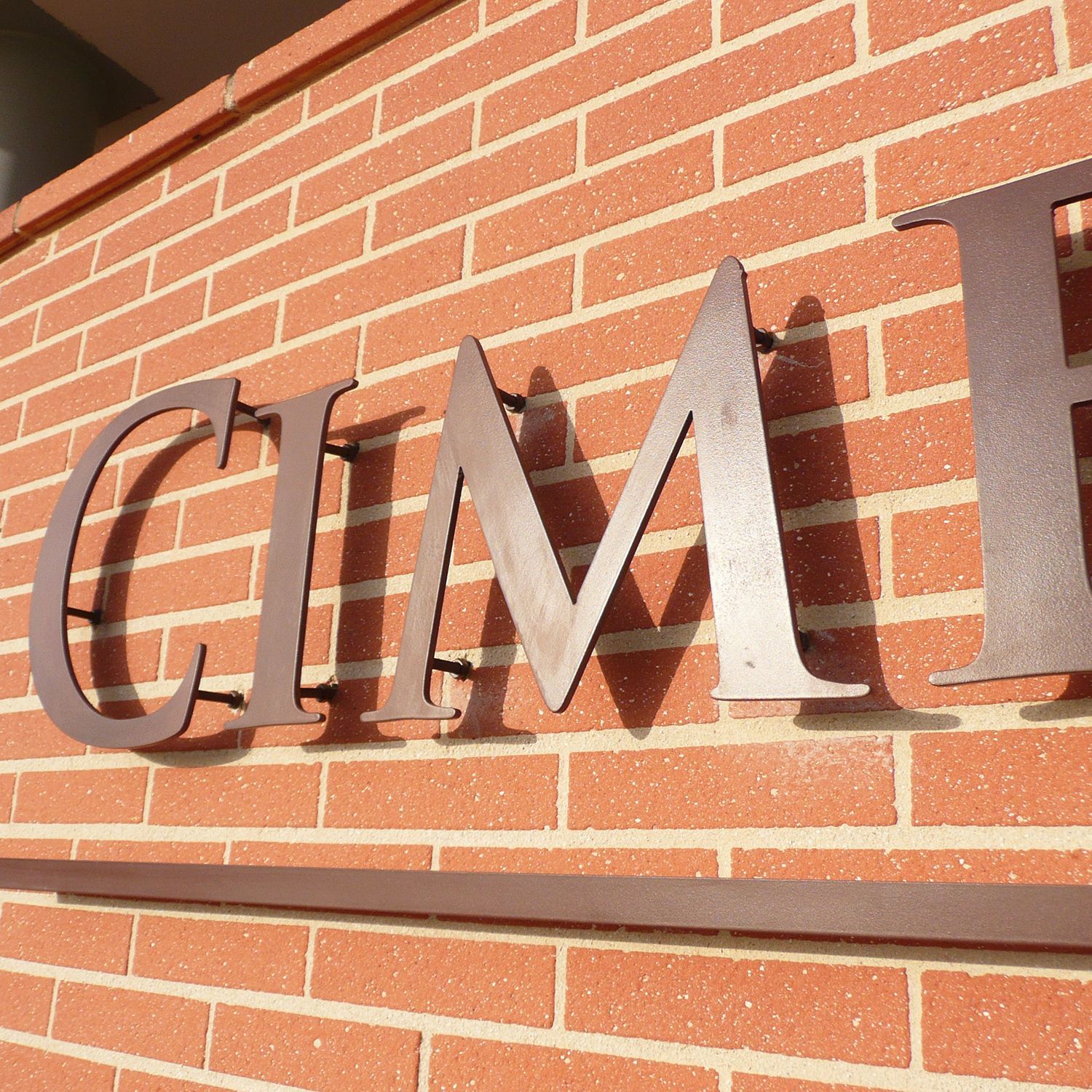 Lettres métalliques CIMP fixées sur un mur de briques rouges au soleil