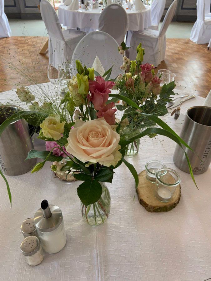 Ein florales Gesteck mit Rosen und Grünzeug auf einem weiß gedeckten Banketttisch in einem Empfangssaal
