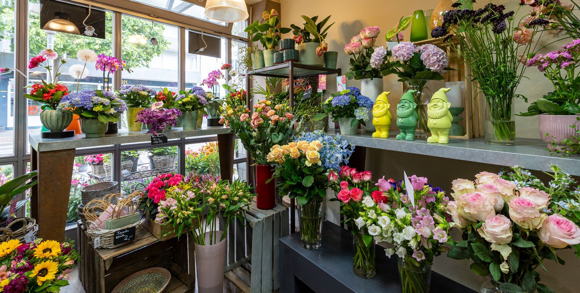 Innenansicht eines Blumenladens mit farbenfrohen Blumensträußen und Topfpflanzen auf Regalen und Tischen.