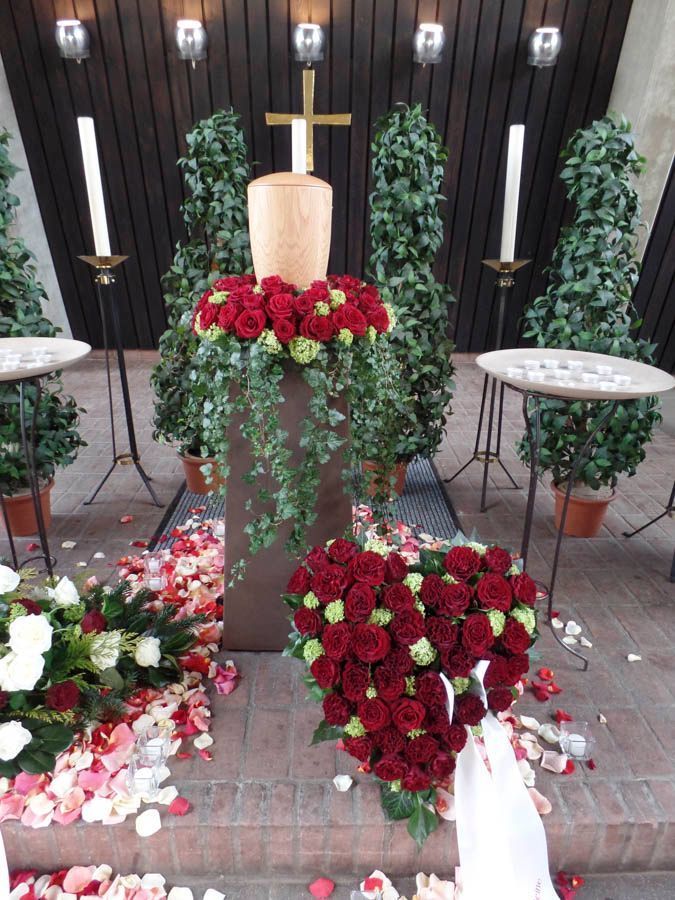 Gedenkaltar mit Kreuz, Kerzen und rot-weißen Blumenarrangements auf einer Stufe vor einer Kirche