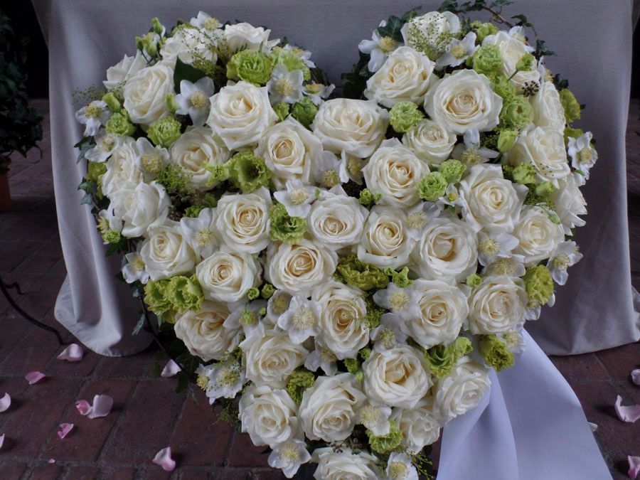 Ein herzförmiger Strauß weißer Rosen mit hellgrünen Akzenten auf einem drapierten Stuhl