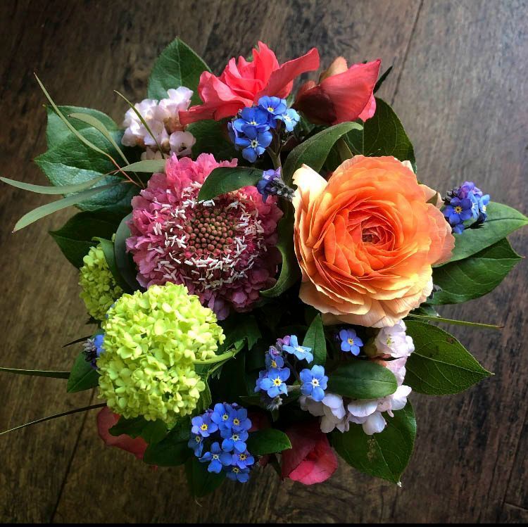 Bunter gemischter Blumenstrauß mit orangefarbenen Rosen, roten und violetten Blüten auf einer Holzoberfläche