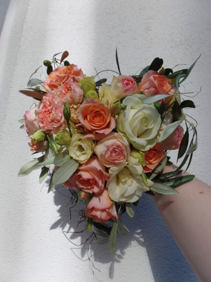 Ein Strauß aus pfirsichfarbenen, cremefarbenen und rosafarbenen Rosen mit Grünzeug vor einer weißen Wand