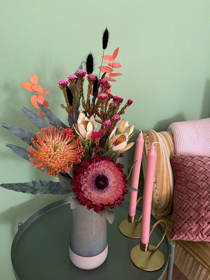 Ein farbenfrohes Blumenarrangement in einer grauen Vase neben rosa und goldenen Kerzen auf einem Tisch.