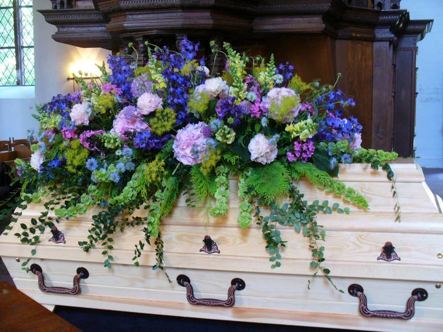 Weißer Sarg, geschmückt mit lila und weißen Blumen in einer Kirchenkapelle