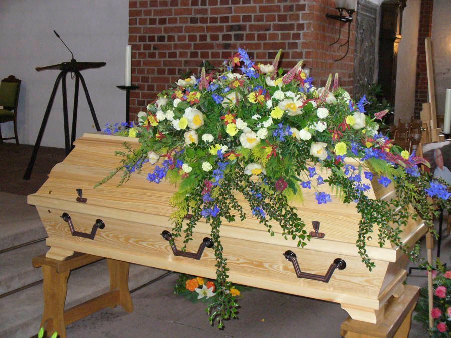 Ein mit einem farbenfrohen Blumenarrangement bedeckter Holzsarg in einer Kirchenkapelle