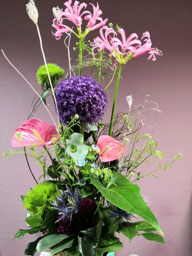 Hohes Blumenarrangement mit rosa Lilien, violettem Zierlauch, grünem Laub und dunklen Blüten in einer Vase