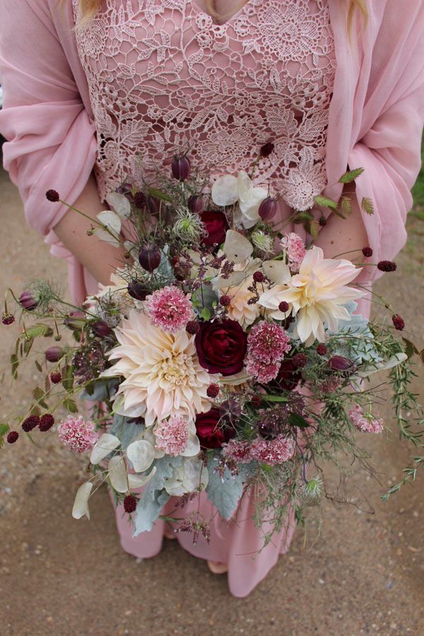 Eine Person, die im Freien einen pastellrosa-weißen Blumenstrauß hält und ein rosa Spitzenkleid trägt.