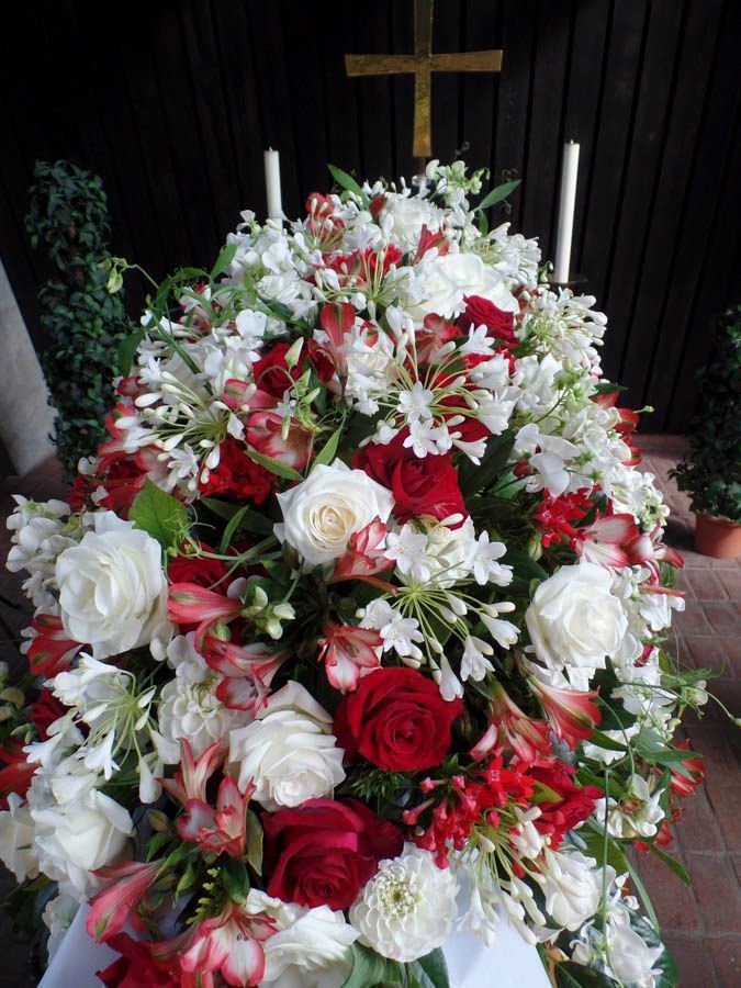 Großes Trauergesteck aus roten, weißen und rosa Blüten unter einem Kreuz auf einem Kirchenaltar