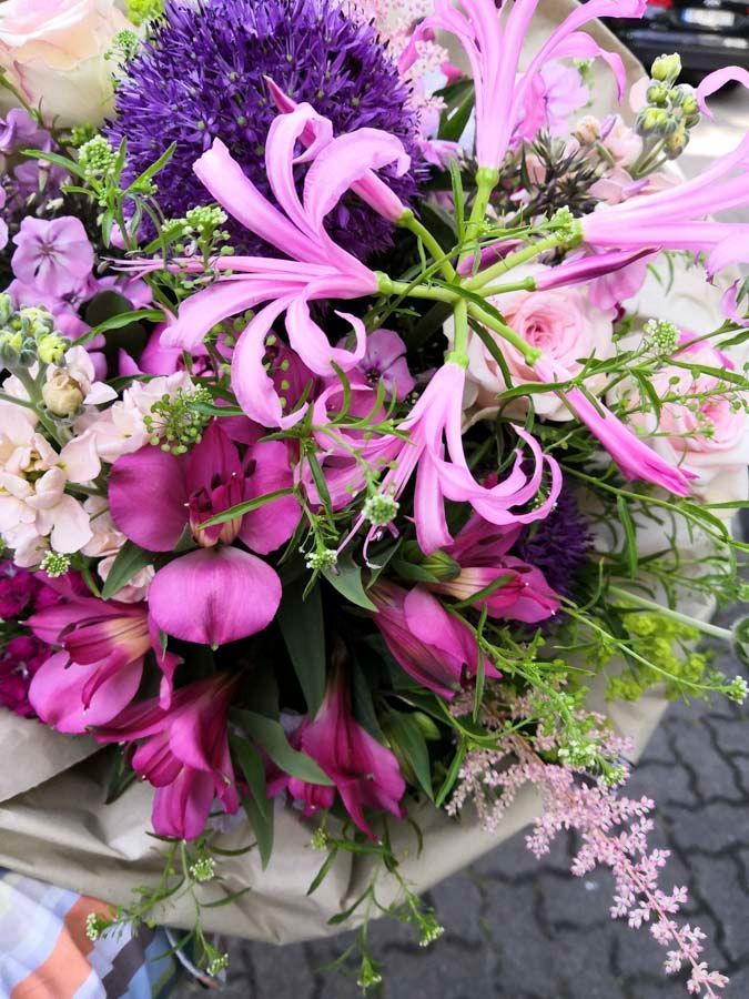 Gemischter Blumenstrauß in Rosa und Lila mit Lilien, Rosen und kleinen weißen Blüten auf grauem Stoff