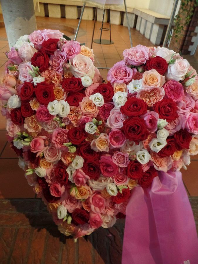 Herzförmiges Arrangement aus rosa, roten und cremefarbenen Rosen mit einem rosa Band auf einem Holzständer