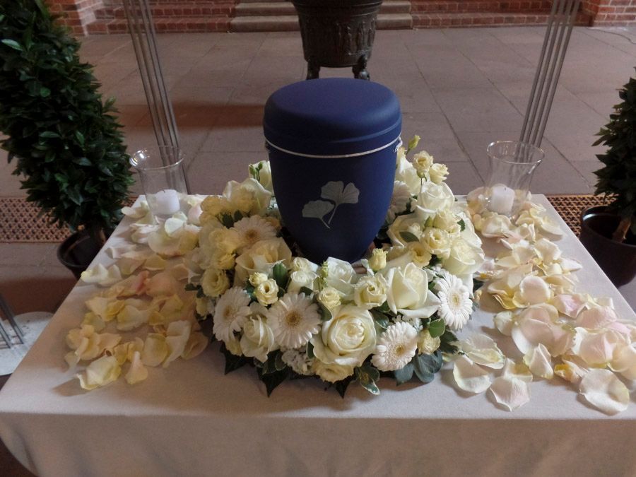 Blaue Urne, umgeben von weißen und hellgelben Blumen auf einem dekorierten Tisch