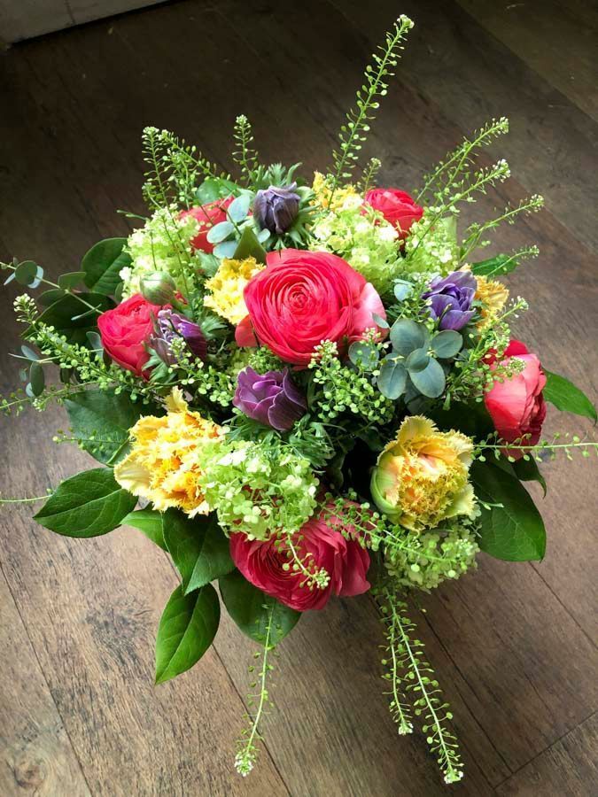 Ein bunter Blumenstrauß aus rosa, gelben, violetten und roten Blüten mit grünem Laub auf einem Holztisch