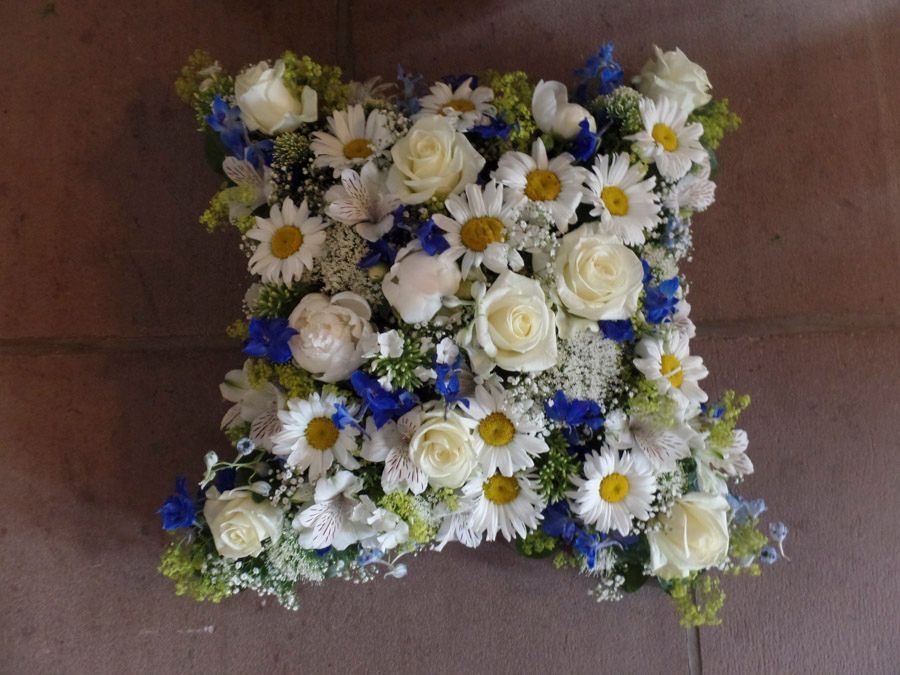 Quadratisches Blumenarrangement aus weißen Rosen, Gänseblümchen und blauen Blumen auf einer Holzoberfläche