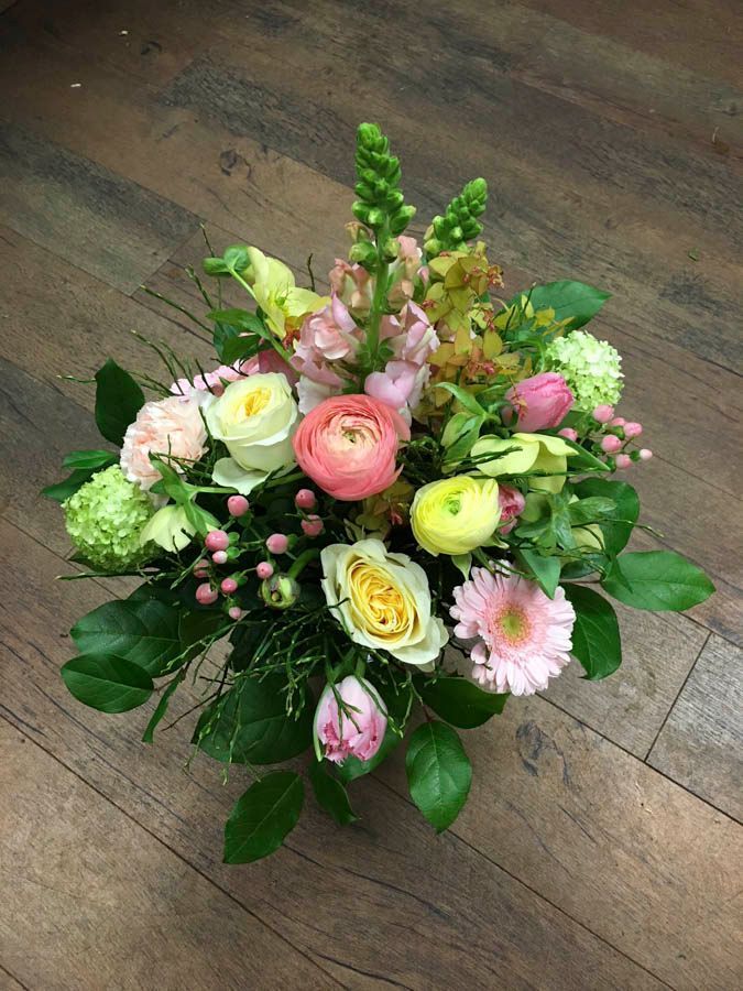 Ein bunter Blumenstrauß aus rosa, weißen, gelben und grünen Blumen auf einem Holzboden