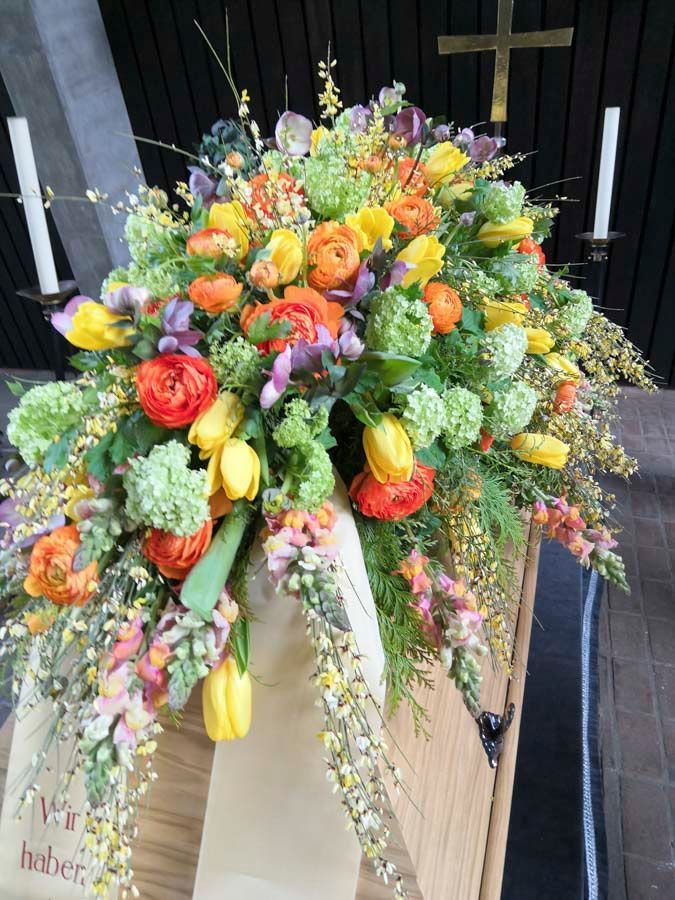Farbenfroher Sargschmuck mit Rosen, Hortensien, Lilien und rankendem Grün in Orange, Gelb und Lila.