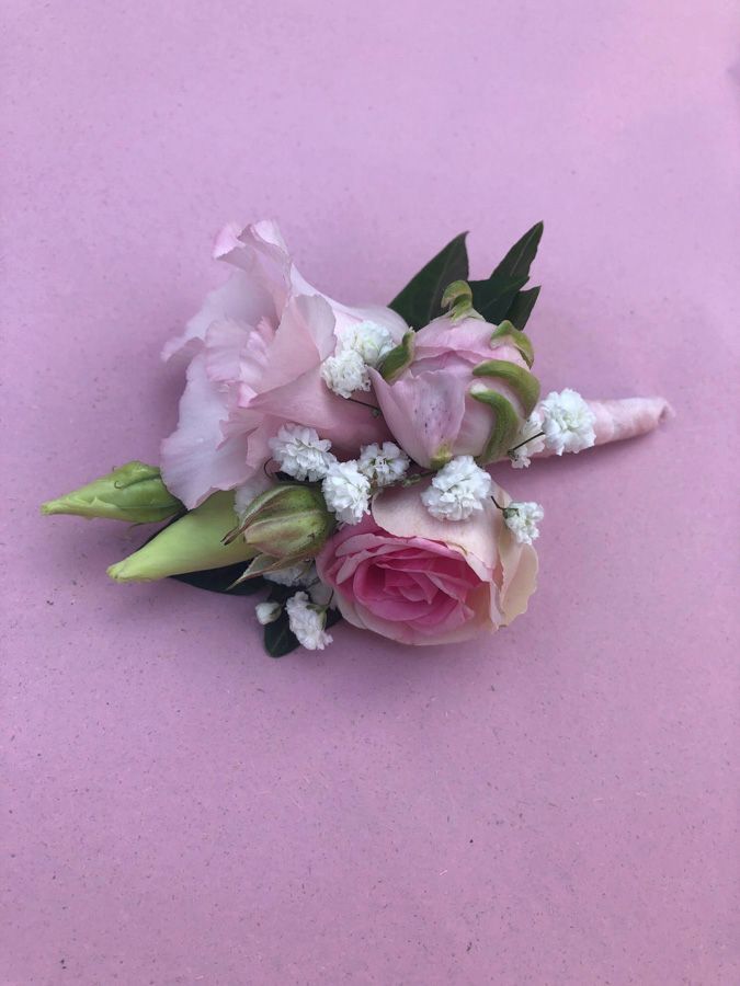 Kleine rosa-weiße Blumenbrosche mit grünen Blättern auf hellviolettem Hintergrund