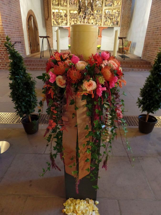 Blumenarrangement mit rosa und orangefarbenen Blumen auf einem Podest im Kirchenraum