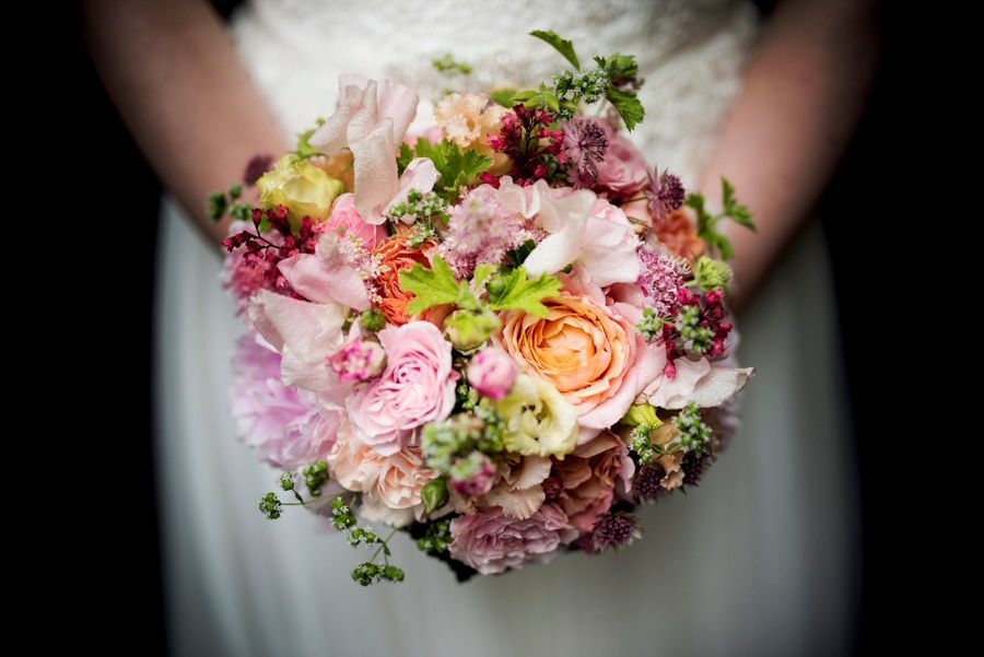 Ein Strauß aus rosa, pfirsichfarbenen und violetten Blumen vor einem weißen Kleid