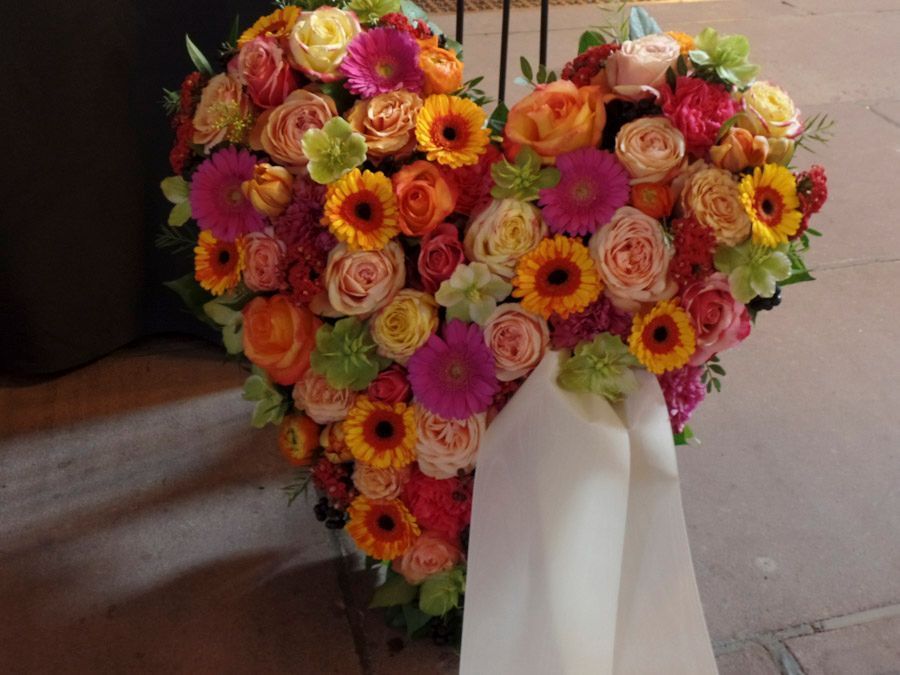 Ein herzförmiger Strauß bunter Blumen mit einem weißen Band ist ausgestellt.