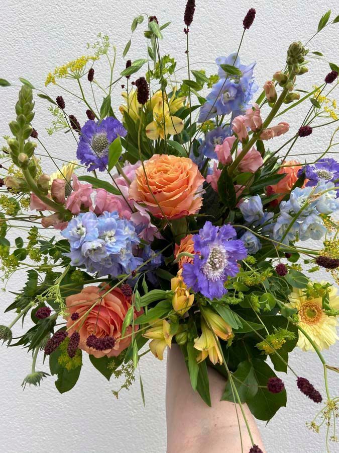 Ein bunter gemischter Blumenstrauß mit Rosen, blauen Hortensien und Grün in einer rosa Vase