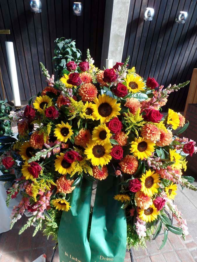Großer Strauß roter, gelber und rosafarbener Blumen in einer grünen Vase an einer Gedenkstätte im Freien