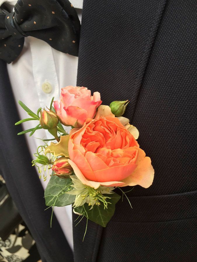 Eine orange und rosafarbene Ansteckblume ist an einem schwarzen Anzugsakko mit weißem Hemd und schwarzer Fliege befestigt.