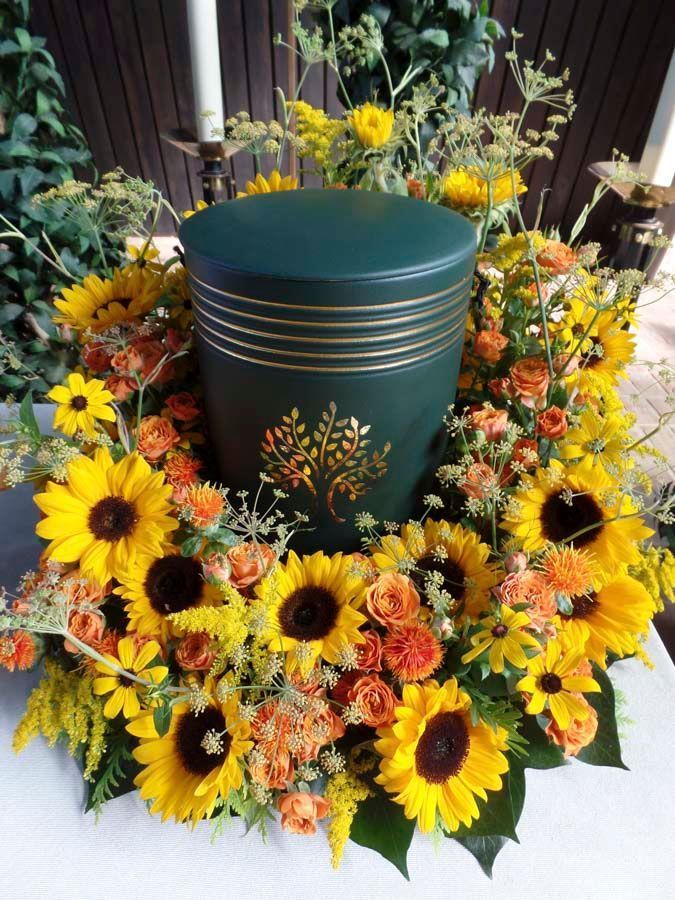 Sonnenblumen und orangefarbene Blüten umgeben ein dunkelgrünes Urnen-Mittelstück