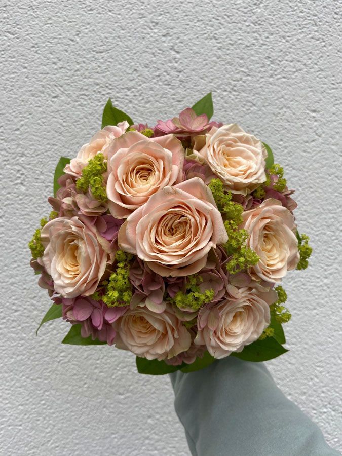 Ein Strauß hellrosa Rosen mit grünen Akzenten vor einer hellgrauen Wand.