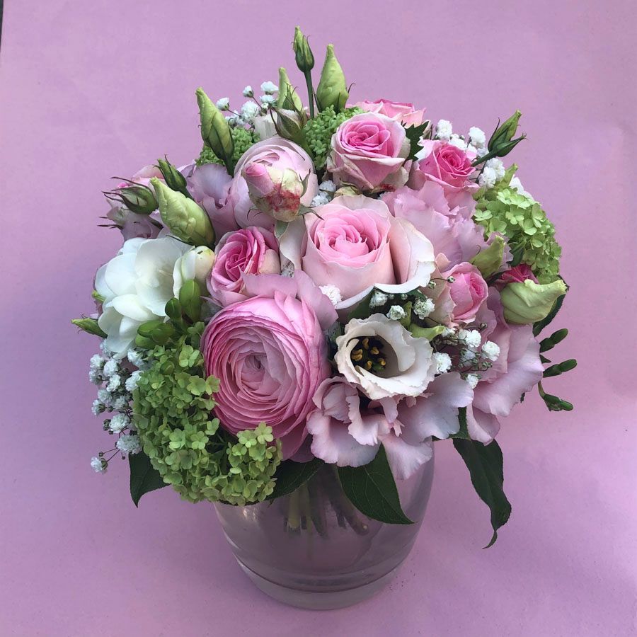 Rosa-weißer Blumenstrauß in einer Glasvase vor lavendelfarbenem Hintergrund